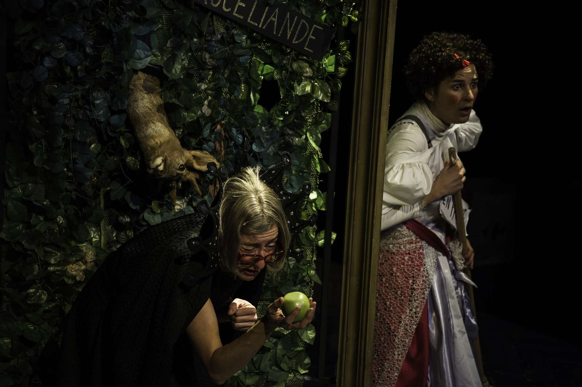Une femme déguisée en vielle femme tient une pomme verte. Une autre femme à côté conte l'histoire.