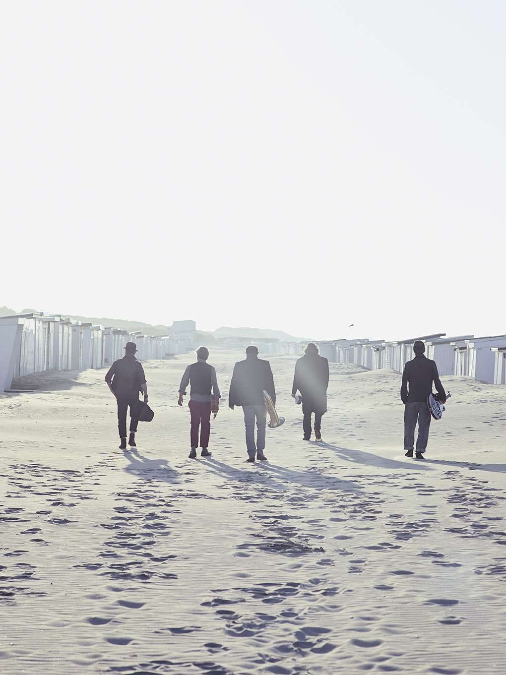Un groupe de musiciens accompagnés de leurs instruments marchent sur le sable.