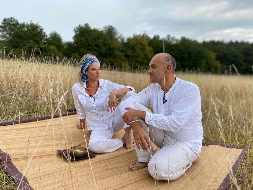 Un homme et une femme vêtus de blanc, sont assis sur un tapis de paille dans un champ de blé.